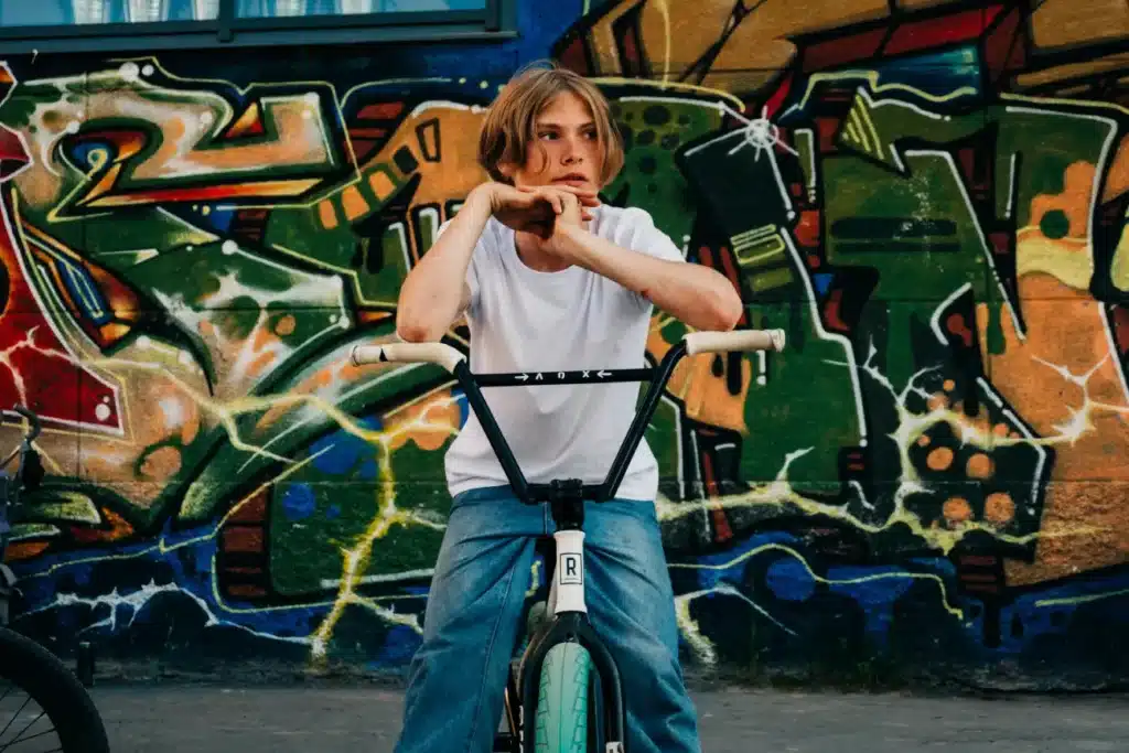 Young Man Sitting on a Bicycle Near Vandalized Wall while Looking Afar